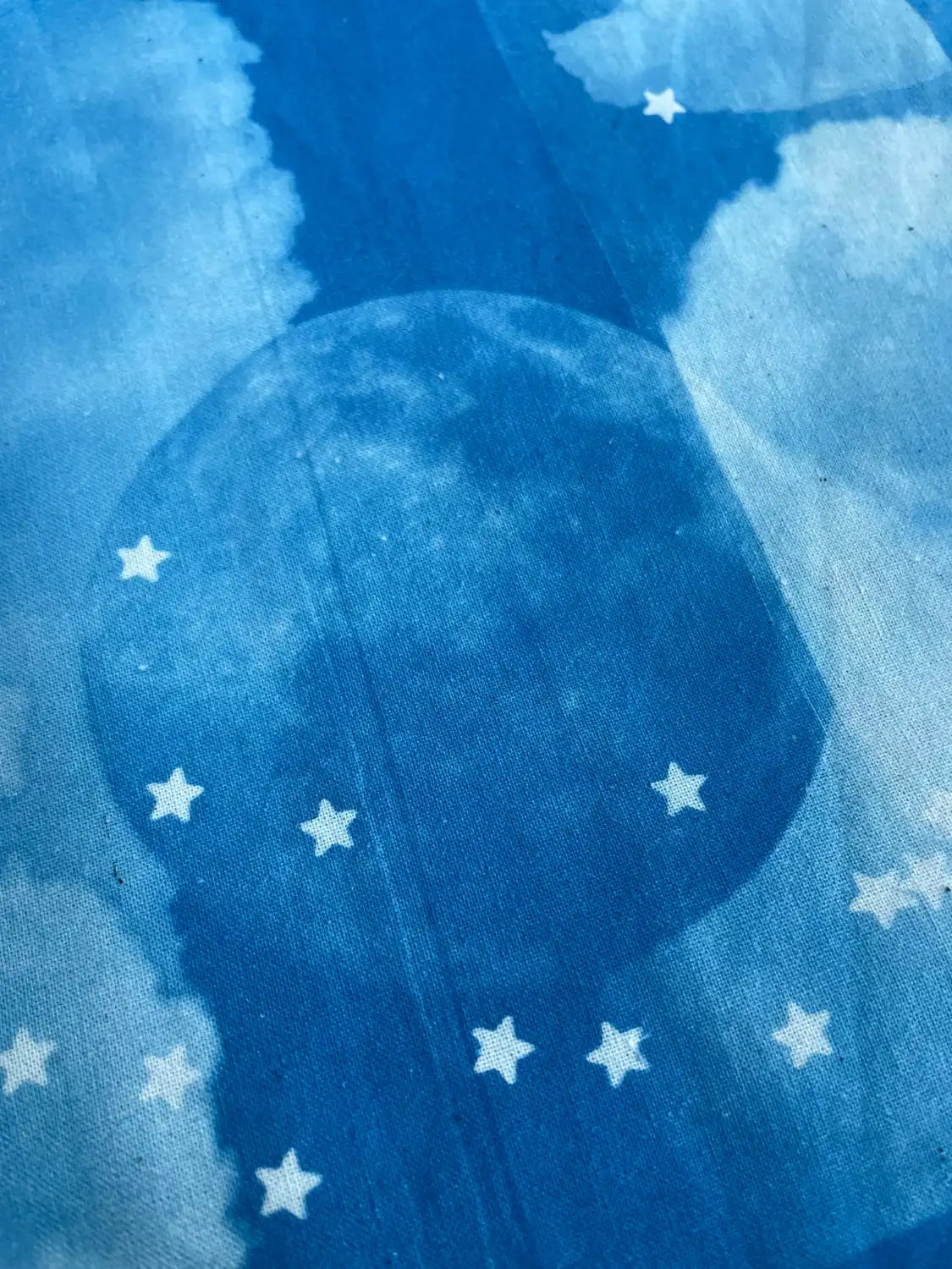 Blue fabric with a celestial print featuring a large moon and scattered white stars, shown in a close-up view.